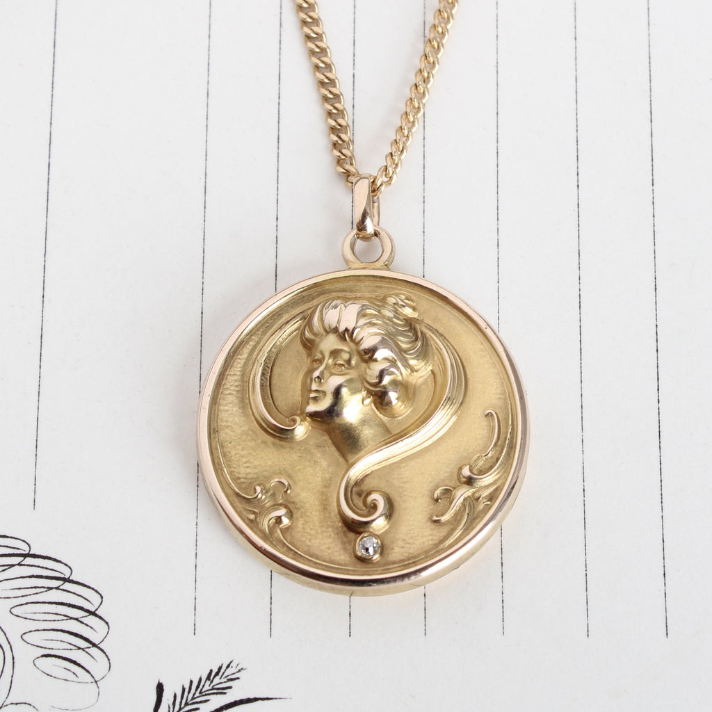 Art nouveau yellow gold round locket with a woman face and single diamond. Hanging on a gold cuban link chain.