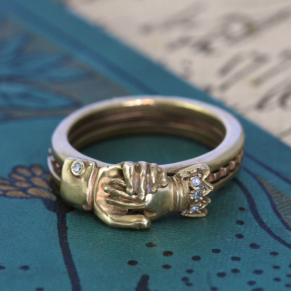 Handmade yellow gold ring with carved hands with diamond studded sleeves interlocked in a handshake.