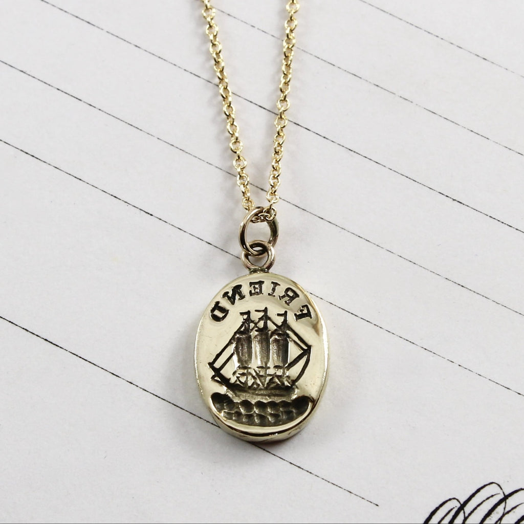 Yellow gold oval pendant with a ship and &quot;FRIEND&quot; carved into the front with patina detailing.