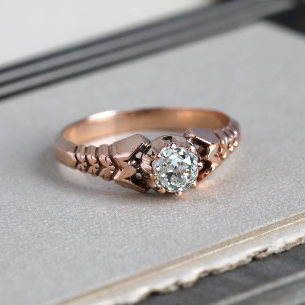Antique rose gold ring with cushion cut diamond and flower carvings on the band.