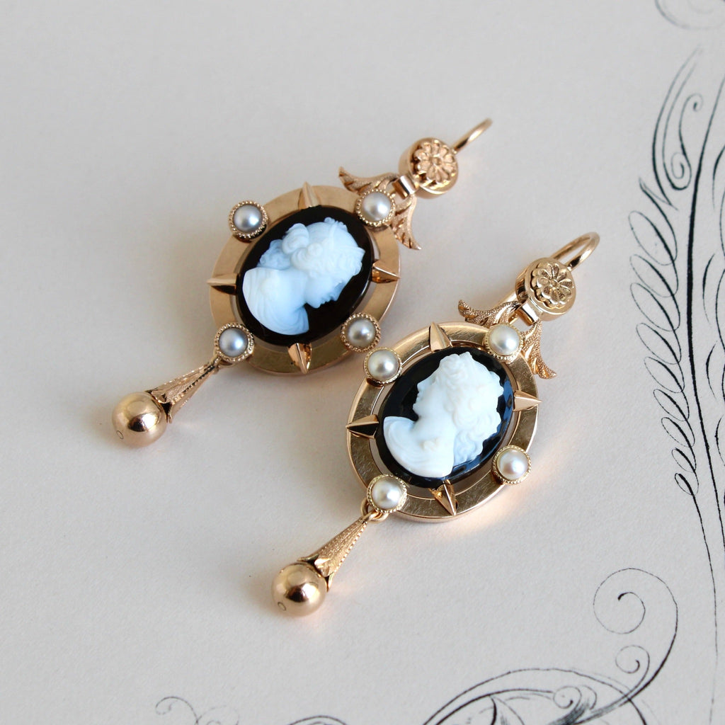 Antique yellow gold dangle earrings with a black and white cameo in an oval bezel studded with pearls and gold drop balls.