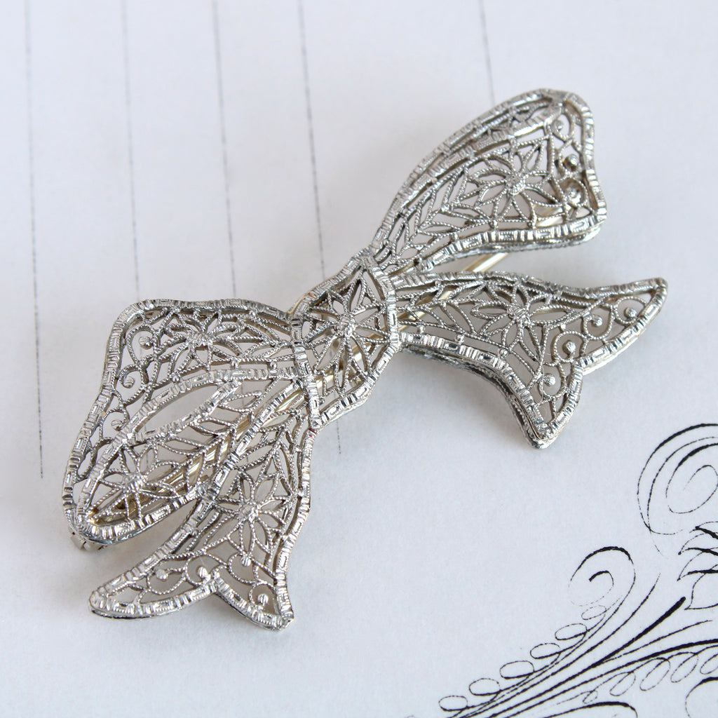 Antique white gold bow pin brooch with filigree designs.