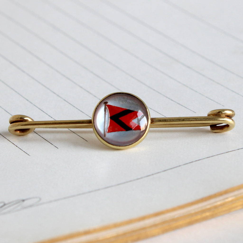 14k yellow gold pin with a red and black nautical flag under a round glass dome.