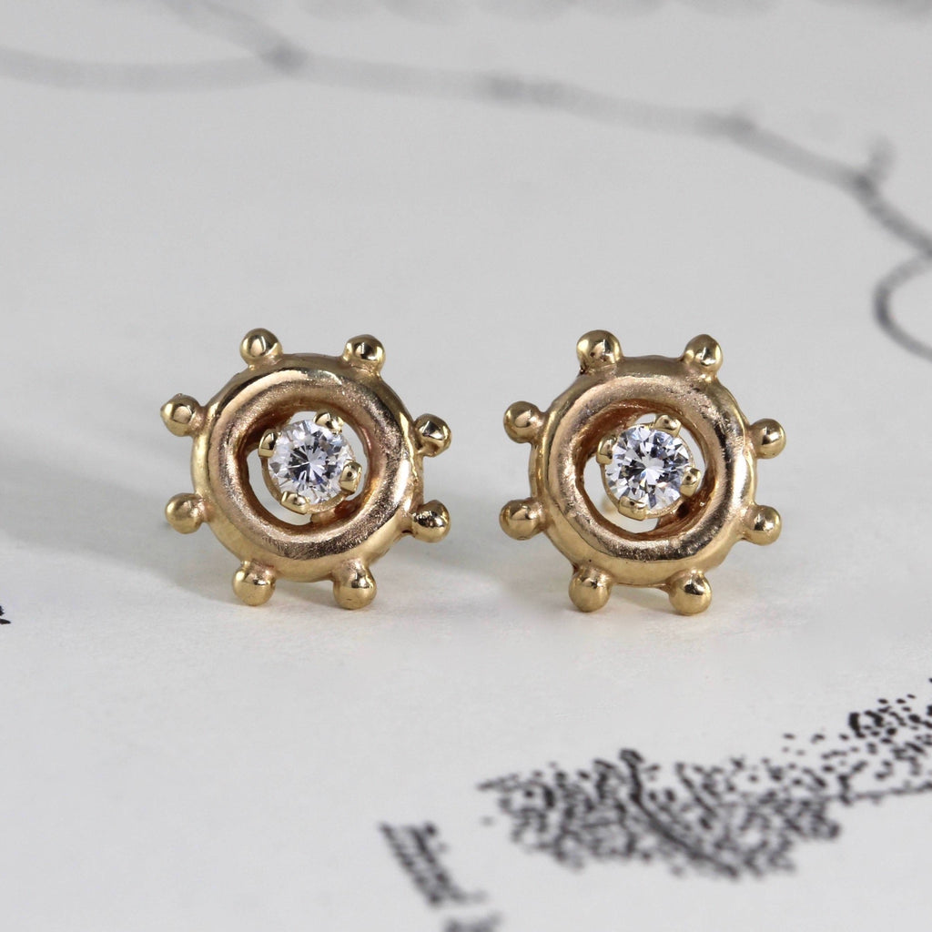 Yellow gold stud earrings in the shape of a ship wheel with round diamonds in the center.