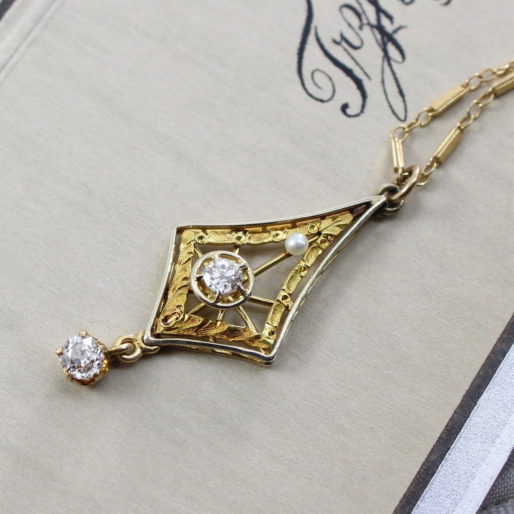 Antique yellow gold lavaliere necklace with a diamond drop, diamond center stone, and fresh water pearl. Hanging on a gold chain.