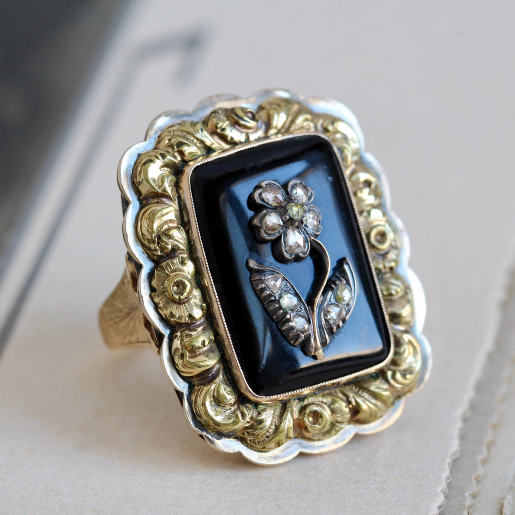 Antique yellow gold statement ring with an onyx cabochon with a sterling silver flower studded with tiny diamonds in a floral style bezel.