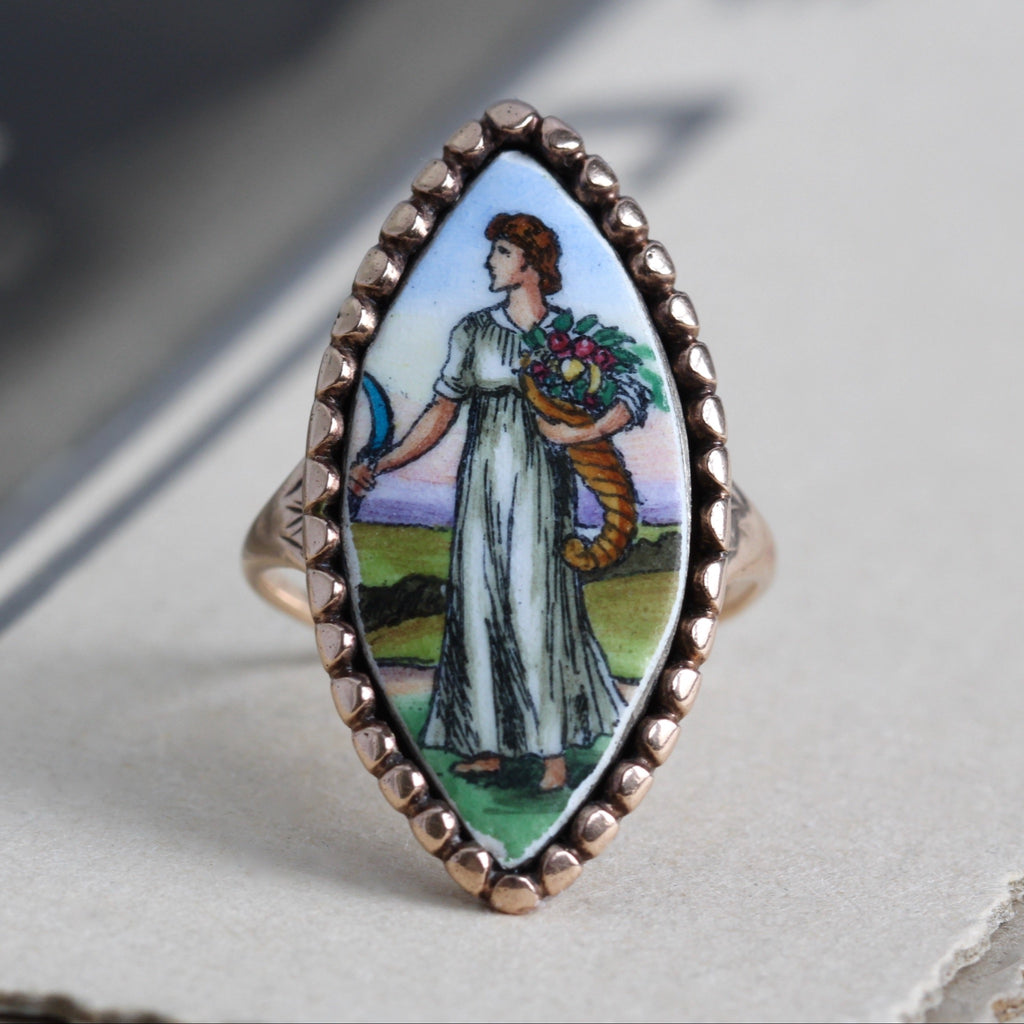 Antique yellow gold ring with a marquis shaped painting of a woman holding a cornucopia with a scalloped bezel.