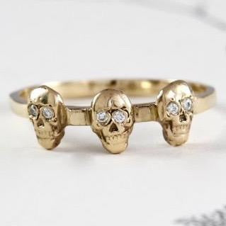 Handmade yellow gold ring with three carved skulls in a row and all with diamond eyes.